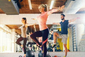 Trainer showing to the group balance exercise in gym. In background their mirror reflection.